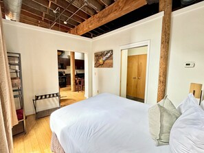 A bedroom with a large bed, wooden beams, a wooden wardrobe, and a kitchen visible through an open door. - Willie (Nashville)