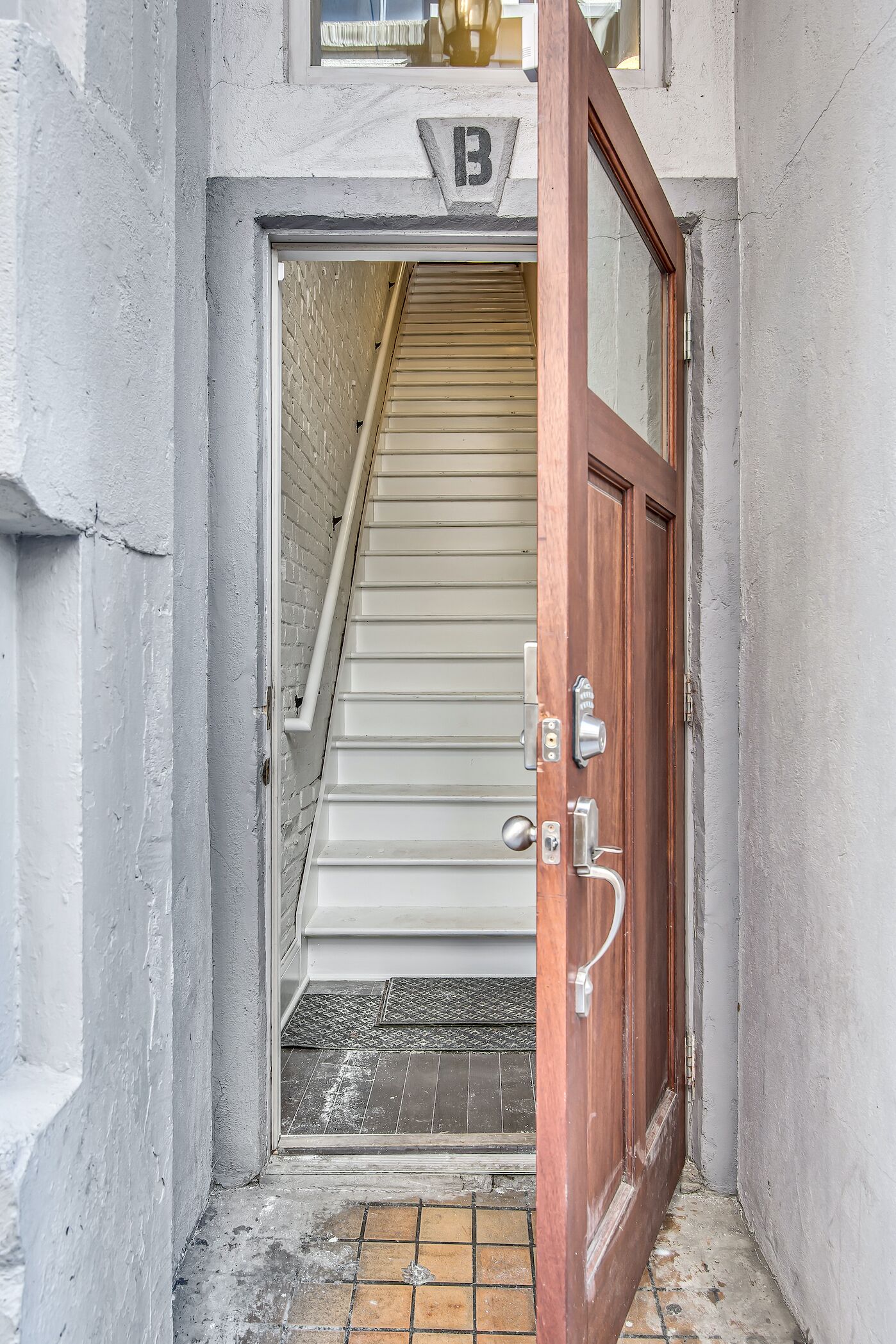 A wooden door with a metal handle and a peephole, leading to a staircase with beige steps.
