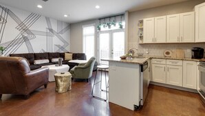 Une cuisine moderne avec des meubles blancs, un îlot central et un coin repas comprenant un canapé en cuir marron et un fauteuil vert.