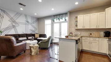Une cuisine moderne avec des meubles blancs, un îlot central et un coin repas comprenant un canapé en cuir marron et un fauteuil vert.
