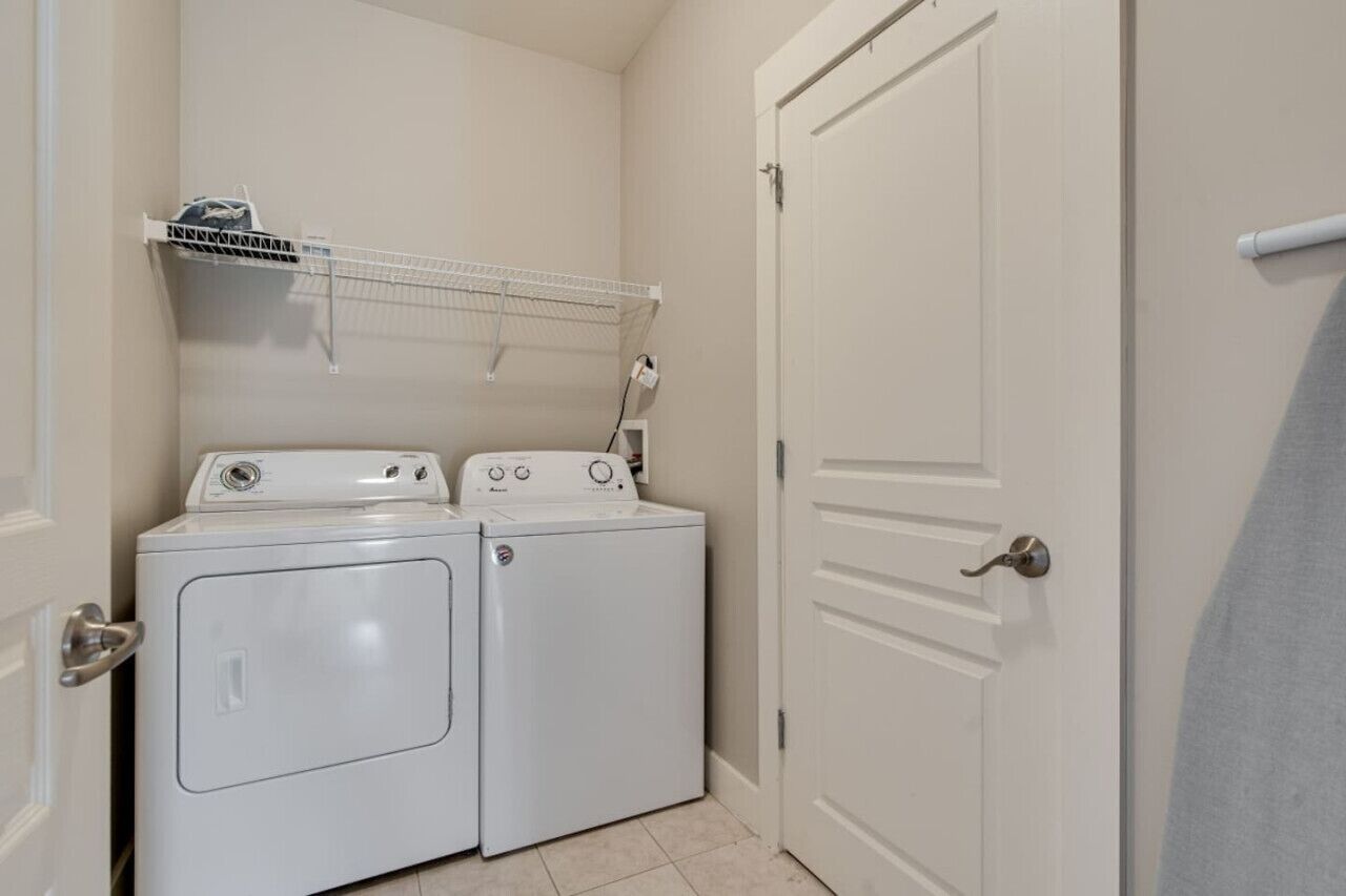 A laundry room with two stacked washers and dryers, a drying rack above, and a white door.