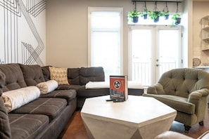 Uma sala de estar com um sofá marrom escuro, uma mesa de centro clara e uma poltrona verde. Há um livro intitulado "The Story of Nashville" sobre a mesa de centro.