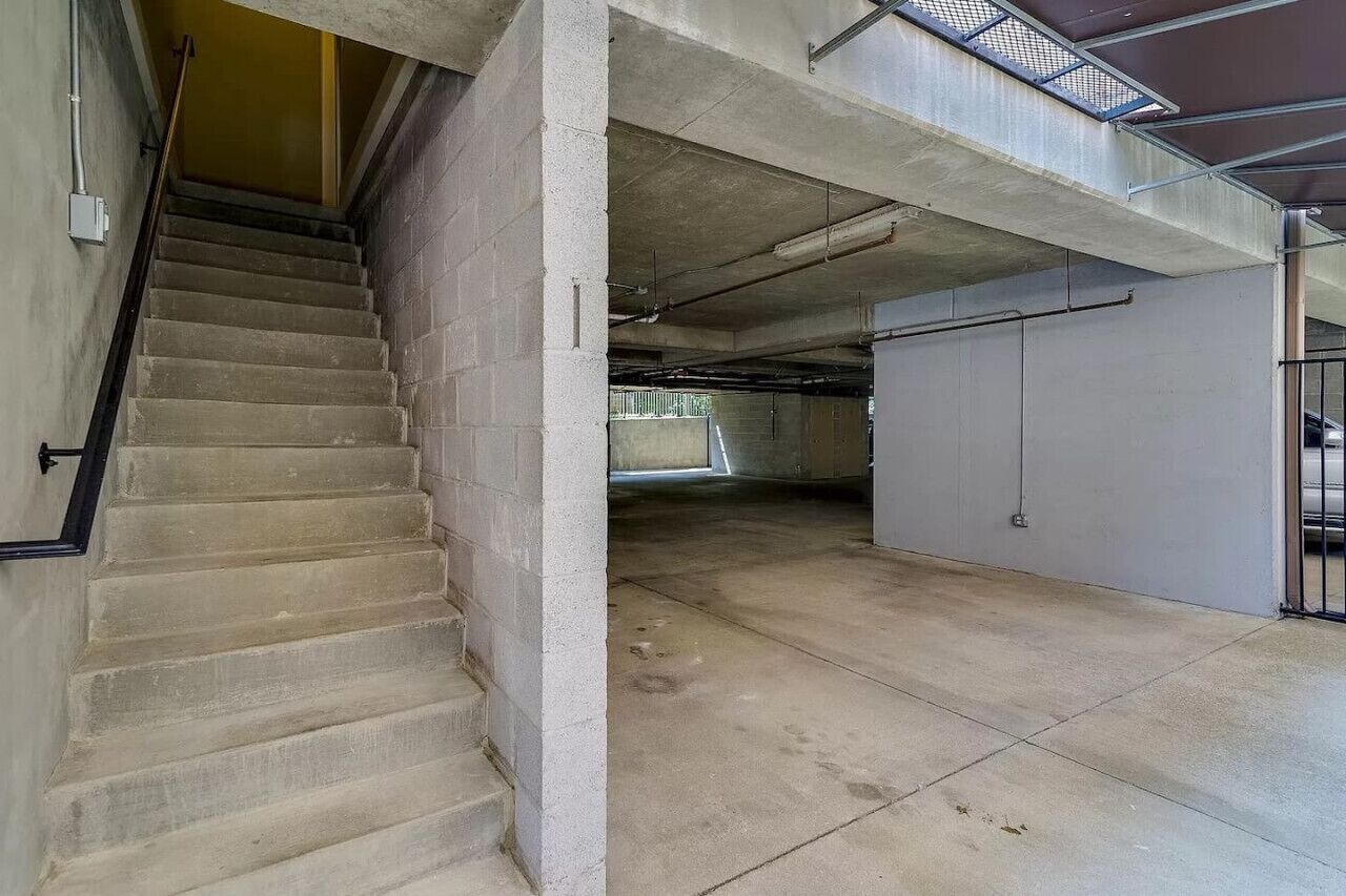 Un escalier en béton menant à un parking, avec une rambarde en métal et une lucarne.