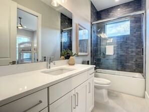A modern bathroom with a glass-enclosed shower, a white toilet, and a vanity with a sink and cabinets. - Lala at the Beach 512 (New Smyrna Beach)