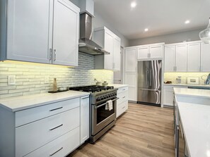 A modern kitchen with white cabinetry, a stainless steel stove, and a built-in oven. - Lala at the Beach 512 (New Smyrna Beach)