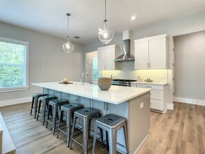A modern kitchen with a large island, bar stools, stainless steel appliances, and pendant lighting. - Lala at the Beach 512 (New Smyrna Beach)