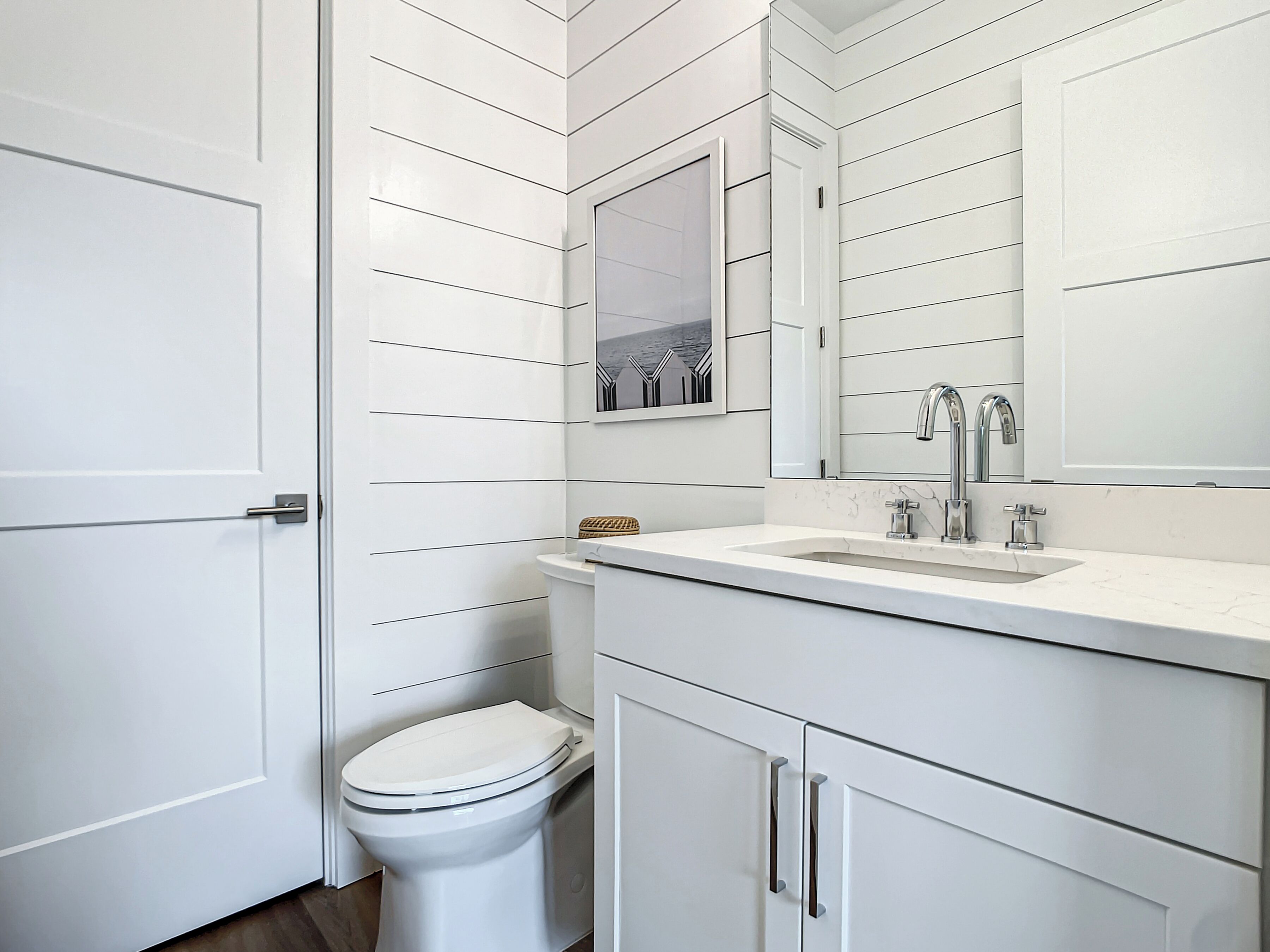 A modern bathroom with white cabinetry, a toilet, a sink with a mirror above it, and a towel rack.