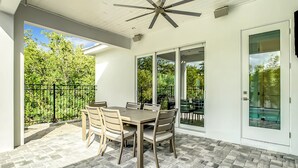 Eine Terrasse mit Tisch und Stühlen, einem Deckenventilator und einer Glastür zum Außenbereich.