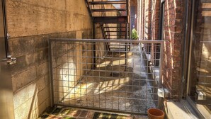 Une ruelle étroite, fermée par un portail en métal, avec des murs en briques et un escalier en bois.