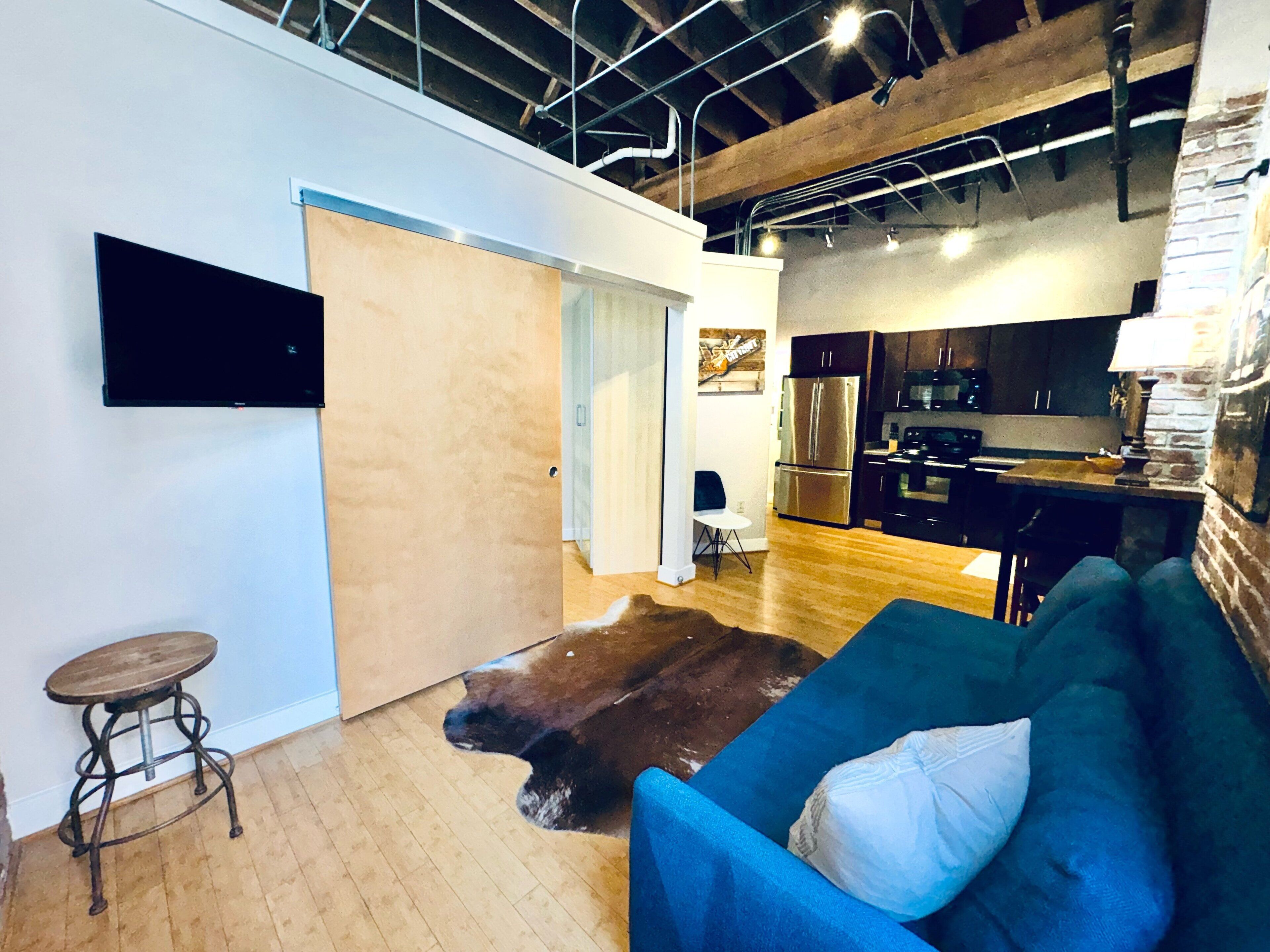 Een moderne keuken met roestvrijstalen apparatuur, een eethoek met een houten tafel en stoelen, en een blauwe bank met een wit kussen.