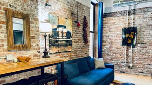 Un salon chaleureux avec un mur en briques, une table en bois, un canapé bleu et un tapis en peau de vache.
