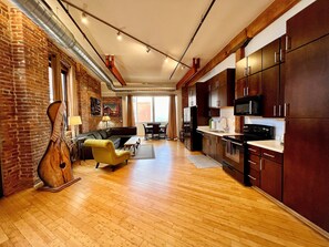 Un vaste espace de vie doté d’un plancher en bois, d’un canapé, d’un fauteuil jaune et d’une table à manger. La cuisine est équipée de meubles en bois foncé et d’un four à micro-ondes.