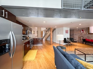 A modern kitchen with a stainless steel refrigerator, wooden cabinets, and a microwave. There is a staircase leading to an upper level. - Elvis (Nashville)