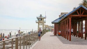 A beach promenade with a lifeguard tower, wooden railings, and a covered seating area. - Oceania Beach Club 504 (New Smyrna Beach)