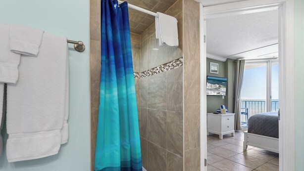 A bathroom with a shower, a towel rack, and a view of a balcony. - Oceania Beach Club 504 (New Smyrna Beach)
