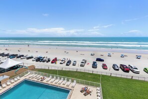 Ein Poolbereich mit Liegestühlen, einem Schwimmbecken und Blick auf Strand und Meer.