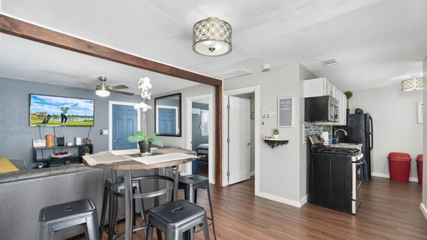 A modern kitchen with a built-in microwave, stove, and sink. There is a dining area with a wooden table and bar stools. The room has a ceiling fan and a decorative light fixture. - Central Phoenix Casita Unit C (Phoenix)