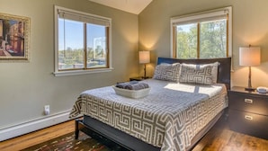 A bedroom with a large bed, two bedside tables with lamps, a ceiling fan, and two windows. - Coach House at Elyon Hall (Gary)