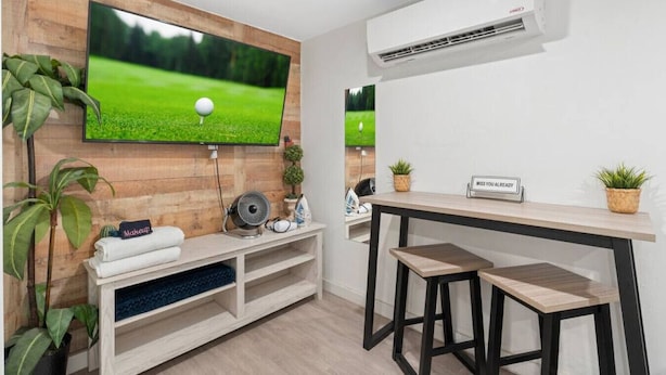 Una habitación moderna con una televisión montada en una pared de madera, una pequeña zona de bar con taburetes y un equipo de aire acondicionado.