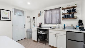 Una cocina compacta con armarios blancos, lavavajillas integrado, un fregadero y una ventana con cortina.
