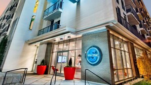 A modern hotel with a prominent neon sign, a glass entrance, and a red potted plant at the entrance. - Spectacular Apartments by BCA Furnished Apartments Spec1b 508 I (Atlanta)