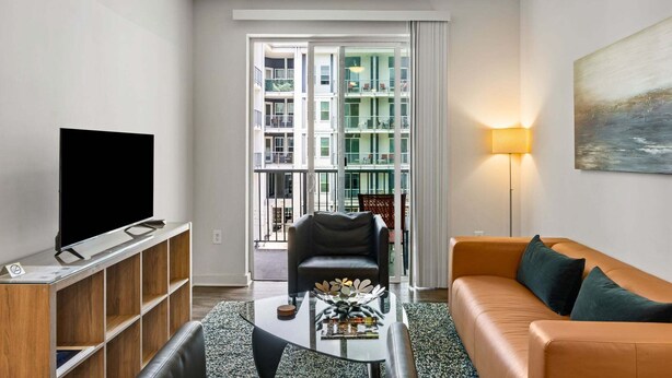 Ein modernes Wohnzimmer mit Flachbildfernseher, Glastisch, Ledersofa und Stehlampe.