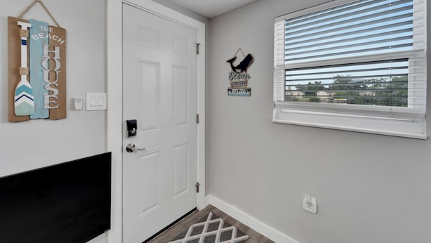 A hallway with a white door, a window with blinds, and wall decorations including a sign that says "The Ocean is Where You Belong." - 8820 Rocky Creek Drive Unit A (Tampa)