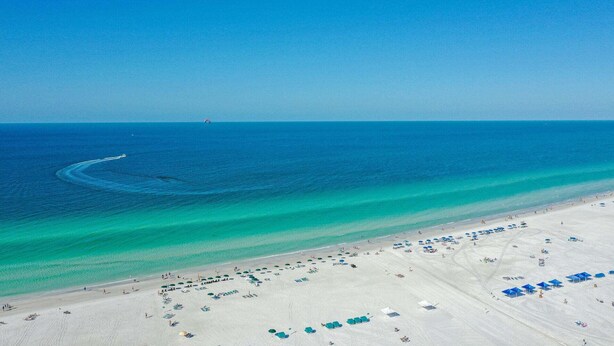 A beach with clear turquoise waters, a sandy shore, and several blue umbrellas. - A Shell House Casa (Siesta Key)