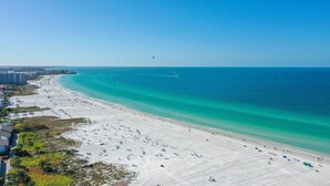 A wide beach with clear turquoise water, a few boats, and a row of buildings along the shore. - A Shell House Casa (Siesta Key)