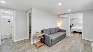 A modern, compact living space with a grey sofa, a wooden side table, and a small plant. - 8820 Rocky Creek Drive Unit B (Tampa)