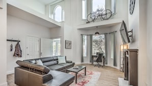 A spacious living room with a sectional sofa, a coffee table, and a fireplace. There are large windows and a high ceiling. - 4632 First Floor Hidden Gem (St. Louis)