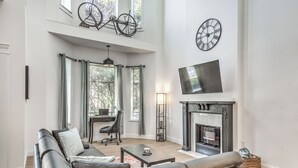 A spacious living room with a fireplace, leather sofas, a television, and a bicycle mounted on the wall. - 4632 First Floor Hidden Gem (St. Louis)