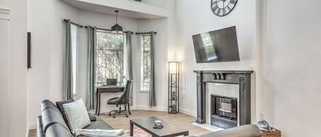 A spacious living room with a fireplace, leather sofas, a television, and a bicycle mounted on the wall.