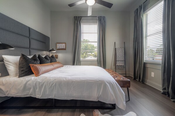 A modern bedroom with a large bed, a ceiling fan, and a view of the outdoors through a window with curtains. - Updated Condo in Heart of Tampa 1569 (Tampa)