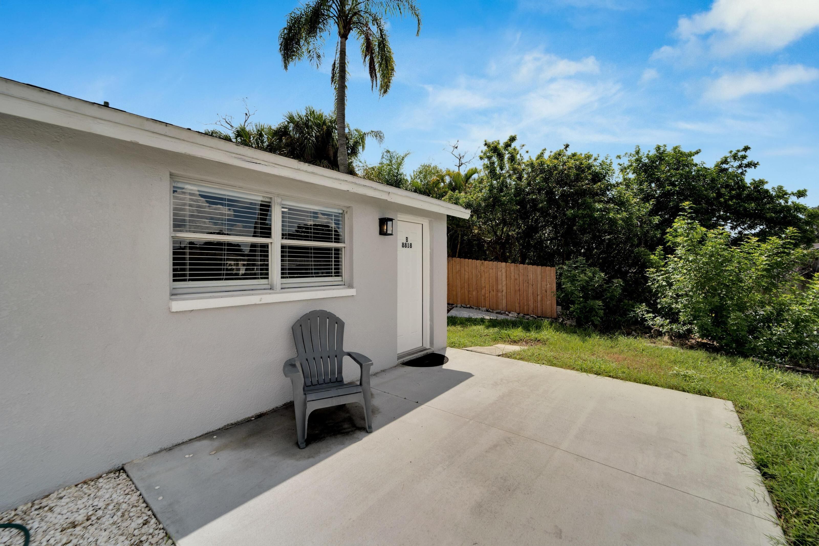 A single-story house with a covered patio, a small chair, and a wooden fence in the background.