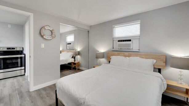 Een moderne slaapkamer met een groot bed, een houten hoofdbord, bedlampen, een ronde spiegel en een ingebouwde oven.