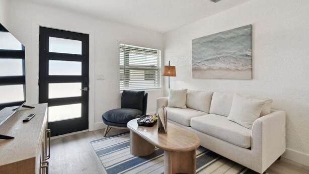 Un salon moderne avec un canapé blanc, une petite table basse, un fauteuil noir, un bureau avec un ordinateur et un grand tableau abstrait accroché au mur.