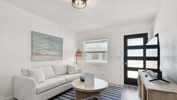 A modern living room with a white sofa, a round coffee table, a lamp, and a door with frosted glass panels. - 1 Bedroom Treasure Island Getaway (Treasure Island)