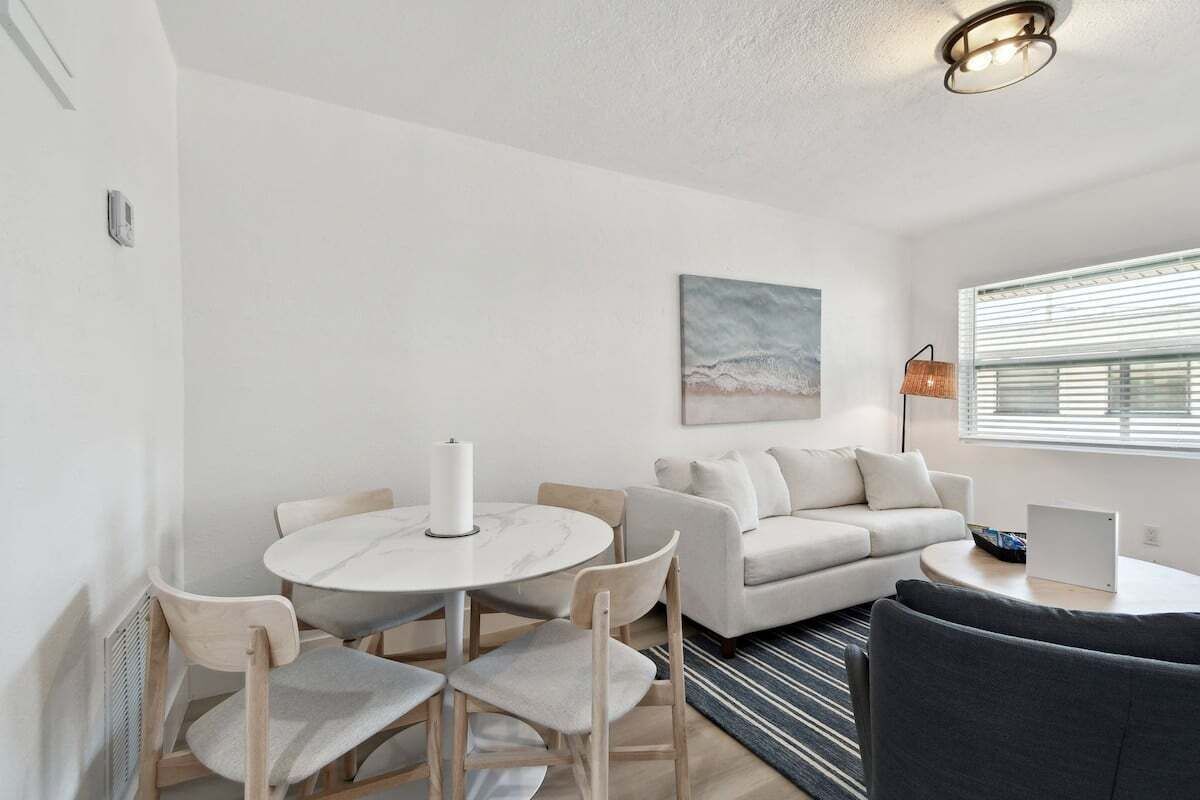 Uma sala de estar moderna com uma mesa de jantar redonda, um sofá e um laptop sobre uma mesinha lateral.