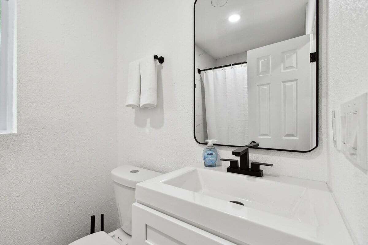 A bathroom with a white sink, a mirror, a toilet, and a shower curtain.