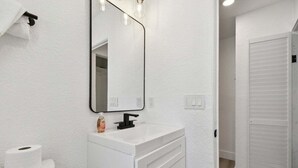Un bagno con un mobile lavabo bianco, uno specchio, un water e una porta bianca.