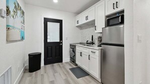Una cocina moderna con armarios blancos, un refrigerador de acero inoxidable y una puerta negra.