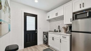 A modern kitchen with white cabinets, a stainless steel refrigerator, and a black door. - New Treasure Island Gem - Unit 3 (Treasure Island)