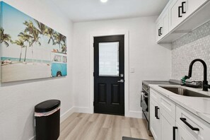 A compact kitchen with white cabinets, a black door, and a painting of a beach scene. - New Treasure Island Gem - Unit 3 (Treasure Island)