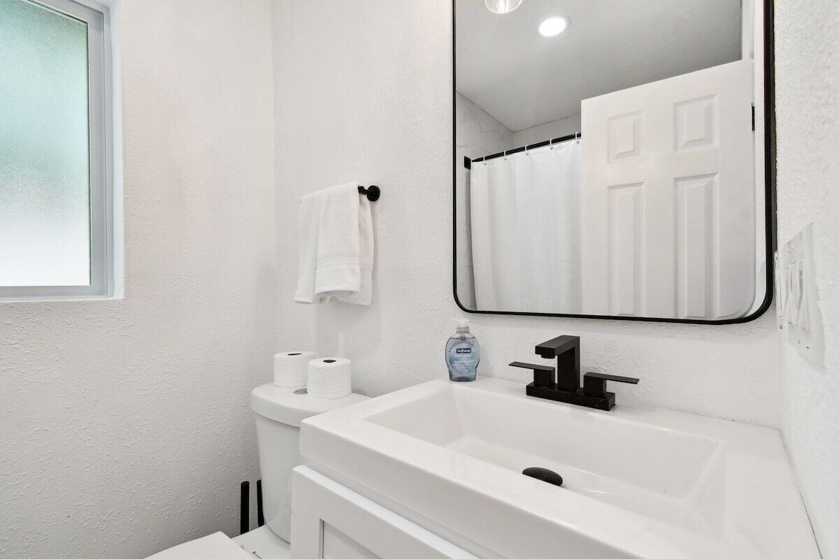 A modern bathroom with a white sink, black faucet, and a mirror above it.
