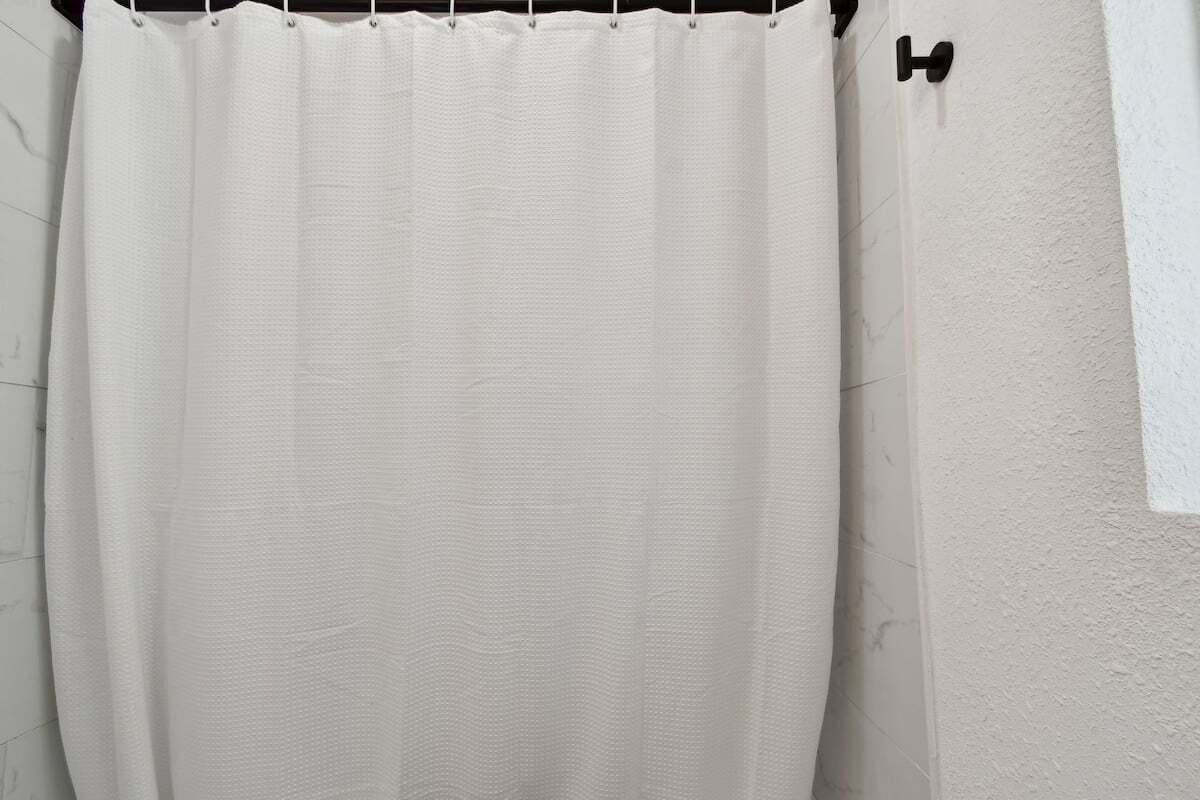 Cortina de ducha blanca con textura, colgada en una barra.