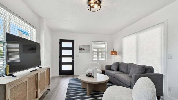 Ein modernes Wohnzimmer mit Flachbildfernseher, grauem Sofa, weißem Sessel und rundem Couchtisch.