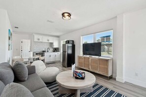 A modern living room with a gray sofa, a round coffee table, and a TV on a wooden cabinet. - Stylish Treasure Island Getaway - Unit 8 (Treasure Island)