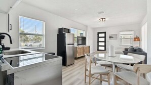 Eine moderne Küche mit einem Edelstahl-Kühlschrank, einer Mikrowelle und einem Spülbecken. Es gibt einen Essbereich mit einem weißen Tisch und Stühlen.