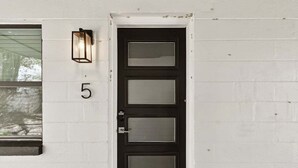 A black door with a number '5' above it, a window to the left, and a wall-mounted light fixture. - Treasure Island Retreat (Treasure Island)